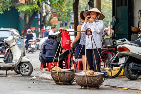 Street vendor with straw hat talking on the phone in a busy street with scooters in the background,
