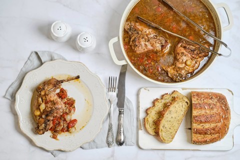 A plate with rabbit stew with vegetables next to a pot filled with more stew. Slices of bread lay