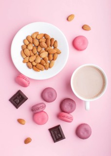 Purple and pink macaron or macaroon cakes with cup of coffee and almonds on pastel pink background.