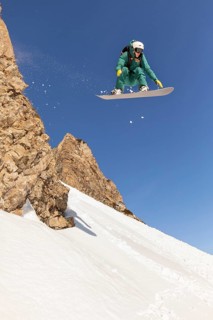 A snowboarder performs an impressive jump over snowy backcountry terrain, showcasing the thrill of