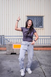 Vertical photo of a cool asian young woman dancing urban music outdoors next to an industrial