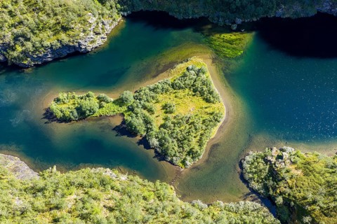 Aerial view of an island in a turquoise colored river surrounded by birch forest, valley