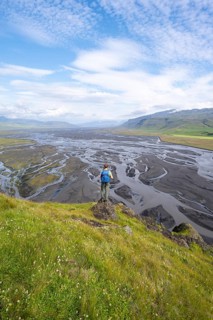 Hiker, young man on a hill, view over alluvial land, meandering river, Dímonarhellir, Suðurland,