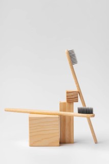 Two bamboo toothbrushes with black bristles are artistically arranged on natural wooden blocks, set