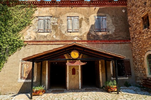 Rustic stone building façade with closed shutters and entrance area, decorative clock, Achaia