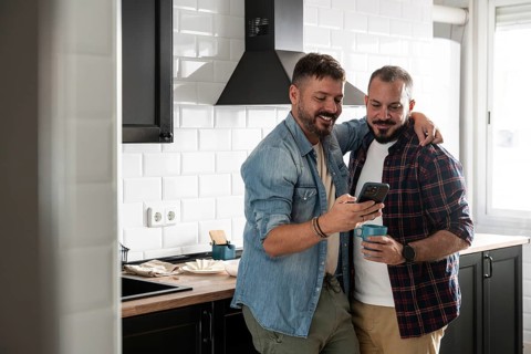 A gay couple shares a tender moment in their modern kitchen. One holds a phone while the other