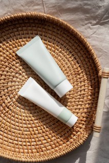Two minimalist skincare cosmetics rest on a woven basket, basking in warm natural light. The simple