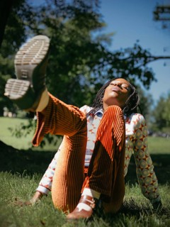 African American woman enjoying a serene moment in nature, lying on the grass with eyes closed,