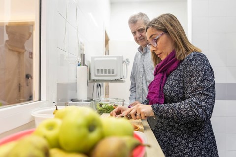A woman chops vegetables in a kitchen, observed by your partner. A focus on fresh ingredients like
