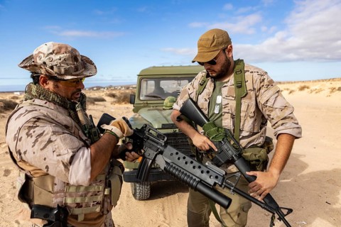 Two soldiers in desert gear, equipped with rifles, prepare for a mission in an arid landscape. They