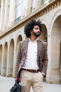 A mixed-race insurance salesman with afro hair stands confidently outdoors, dressed in a plaid