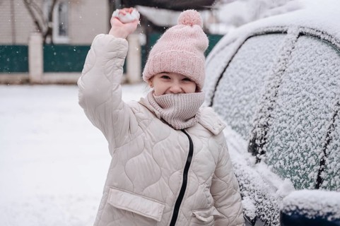 A cheerful girl in a pink hat and white coat plays winter games in snowy Belarus, embodying joy and