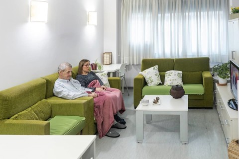 Couple with intellectual disabilities sitting comfortably on a green couch in a supervised home,
