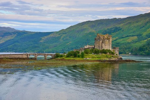 An idyllic scene with a riverside castle and green hills in the background, Eilean Donan Castle,