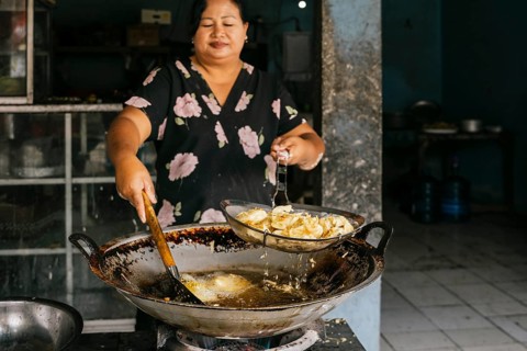 Woman expertly fries in hot oil using a large wok. The scene captures a traditional cooking