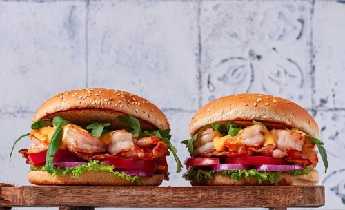 Two shrimp burgers and buns with sesame seeds, bacon, lettuce, tomatoes and onions, On a wooden