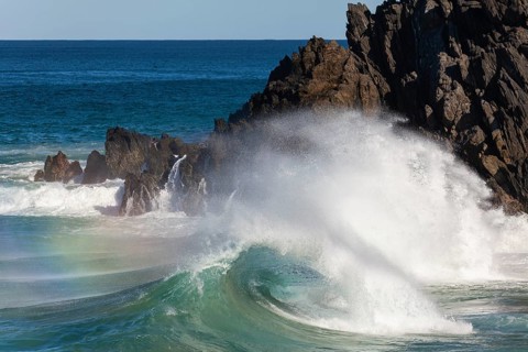 Waves crash against rocks at the mainland's easternmost point, creating rainbows in the ocean spray
