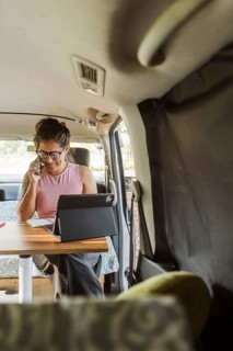 A woman enjoys remote work inside a cozy van during autumn in New Zealand. The setup includes a