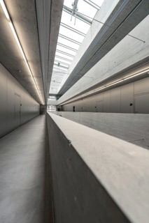 Long and slender corridor in minimalist concrete style, flooded with natural light, University of