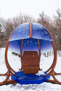 Interactive cocoon rocking chair made of curved wood and backlit blue tinted plexiglass panels