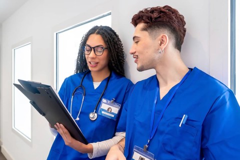 Young medical professionals wearing blue scrubs and stethoscopes, discussing information on a