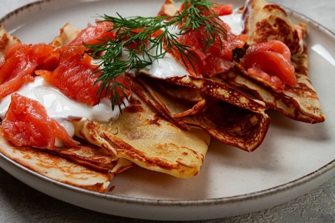 Delicious pancakes with salmon and sour cream, breakfast, on a plate, rustic style, with cutlery