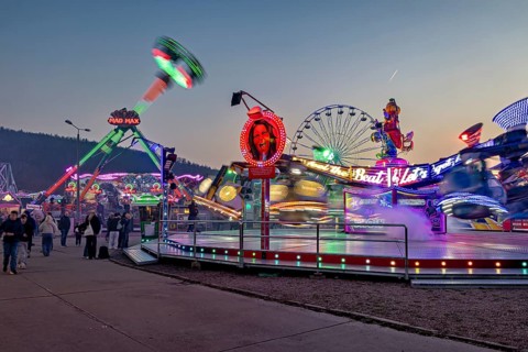 Moving rides and colorful lights at a busy fair at dusk, carousel and hustle and bustle of summer