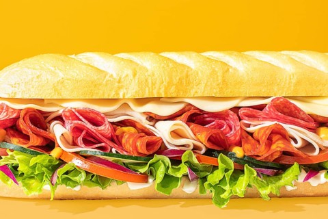 Close-up of a stacked deli sandwich, styled on a vibrant monochrome backdrop, with frontal lighting