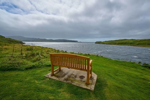 Wooden bench overlooking sea surrounded by green meadow and cloudy sky, Isle of Skye, Scotland,