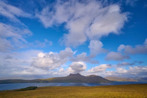 View of a lake surrounded by rolling hills under a vast blue, cloudy sky, Little Loch Broom view