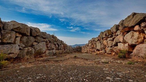 Path between high stone walls with a view of blue sky and distant mountains, Tiryns, ancient city