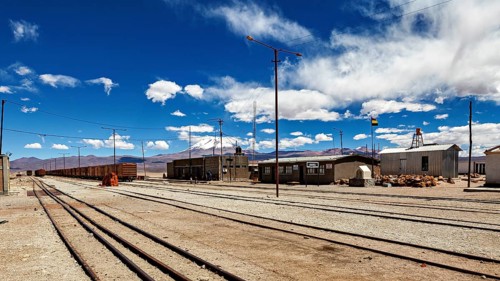 Lonely train stop with scattered buildings and clouds in the sky in front of a mountain range, the