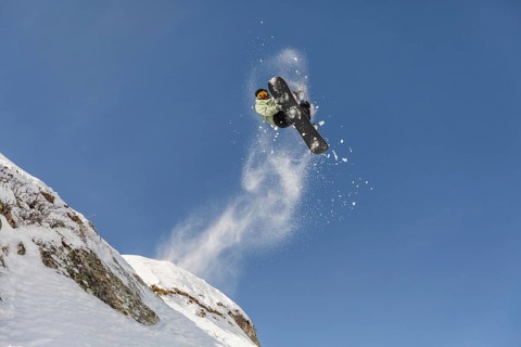 A dynamic image of a freeride snowboarder soaring through the air against a clear blue sky. Snow