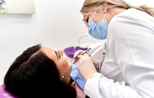 A dentist wearing protective gear examines a patient's teeth in a modern dental clinic. The focus