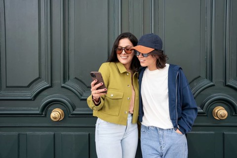 A cheerful lesbian couple takes a selfie together, standing close with smiles, dressed casually in