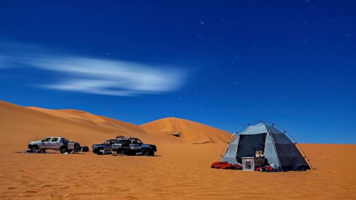 Lonely tent and cars in a quiet dune landscape on a clear night under the starry sky, tent camp in
