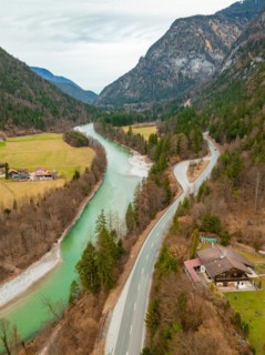 Aerial view of a winding Saalach river next to a road with surrounding forest and mountains under a
