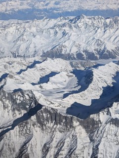 An aerial perspective reveals a breathtaking scene of rugged, snow-covered mountains, with sharp