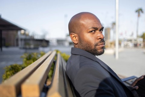 A cuban man in a suit sits on a bench in an urban environment, looking thoughtfully into the