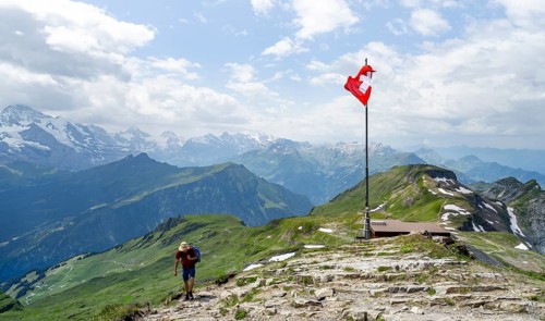 Hikers next to Swiss national flag at the summit of Faulhorn, mountain panorama with Eiger, Mönch