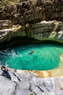 A canyoneer floats peacefully in a vibrant turquoise pool surrounded by curved canyon walls in