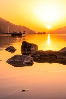 Sunset over a quiet lake with rocks in the foreground and warm light, Großer Alpsee, Immenstadt im