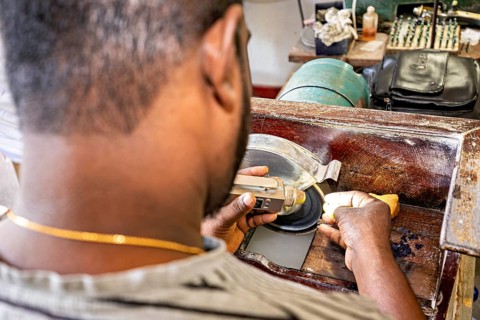 A craftsman works on a piece of jewelry with a grinding machine, focusing on precision, The