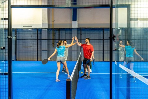 Four enthusiastic players giving high fives after a pickleball match on a bright blue indoor court,