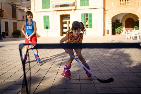 Two children playing roller hockey on roller blades in a sunny urban plaza, displaying joy and