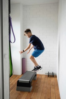 Young boy performing energetic exercises on a step platform indoors. He demonstrates strength and