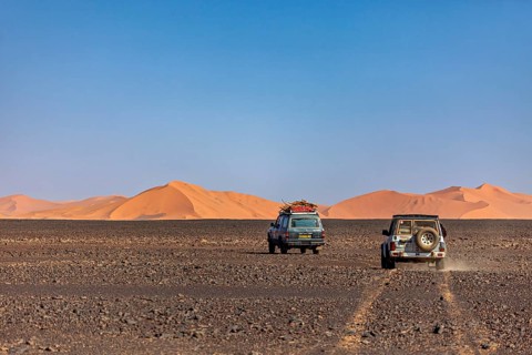 Two off-road vehicles driving in a wide desert landscape with visible sand dunes, Off-road vehicles