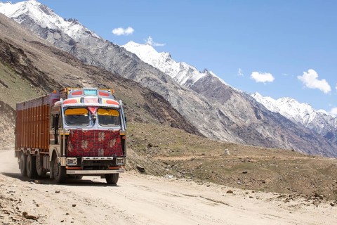 A colorful truck traverses the rugged landscape of Zanskar Valley in Ladakh, India. Snow capped