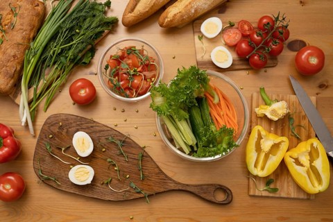 A variety of fresh vegetables, hard-boiled eggs, and whole-grain bread on a wooden table.