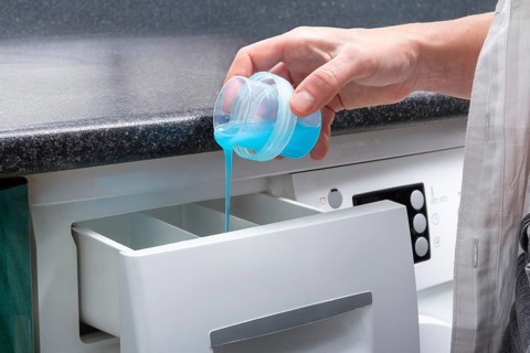 A close-up view of a Gen-Z girl pouring vibrant blue liquid detergent into a front-loading washer